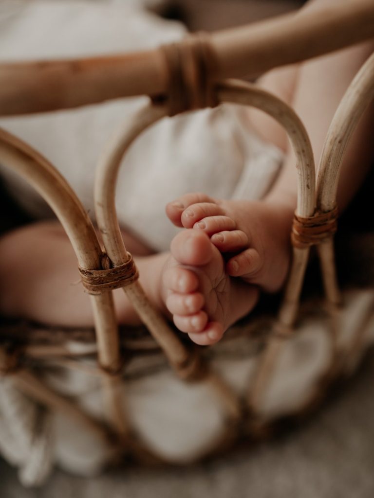 Kleine Babyfüße ragen aus einem geflochtenen Babykorb