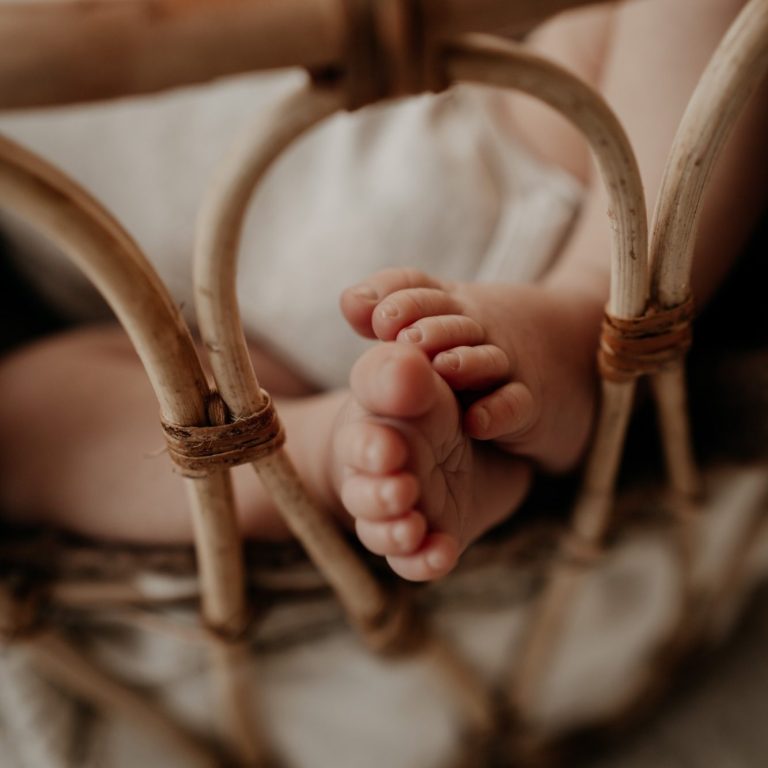  Kleine Babyfüße ragen aus einem geflochtenen Babykorb