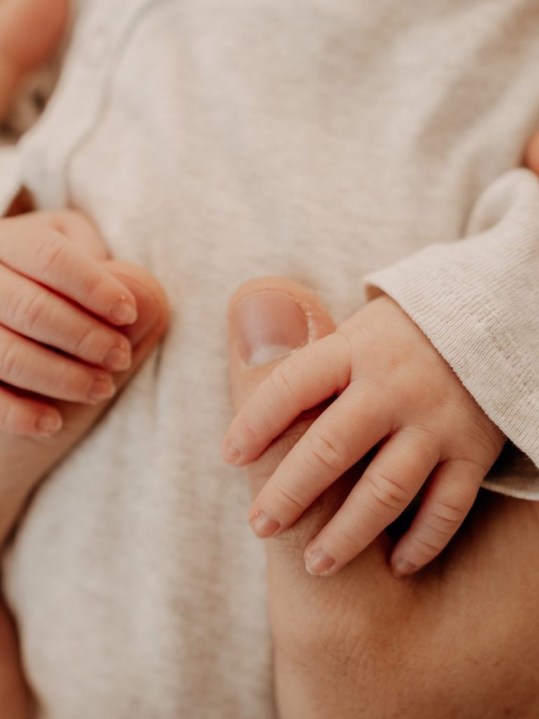 Babyhand greift schützend nach dem Finger eines Erwachsenen